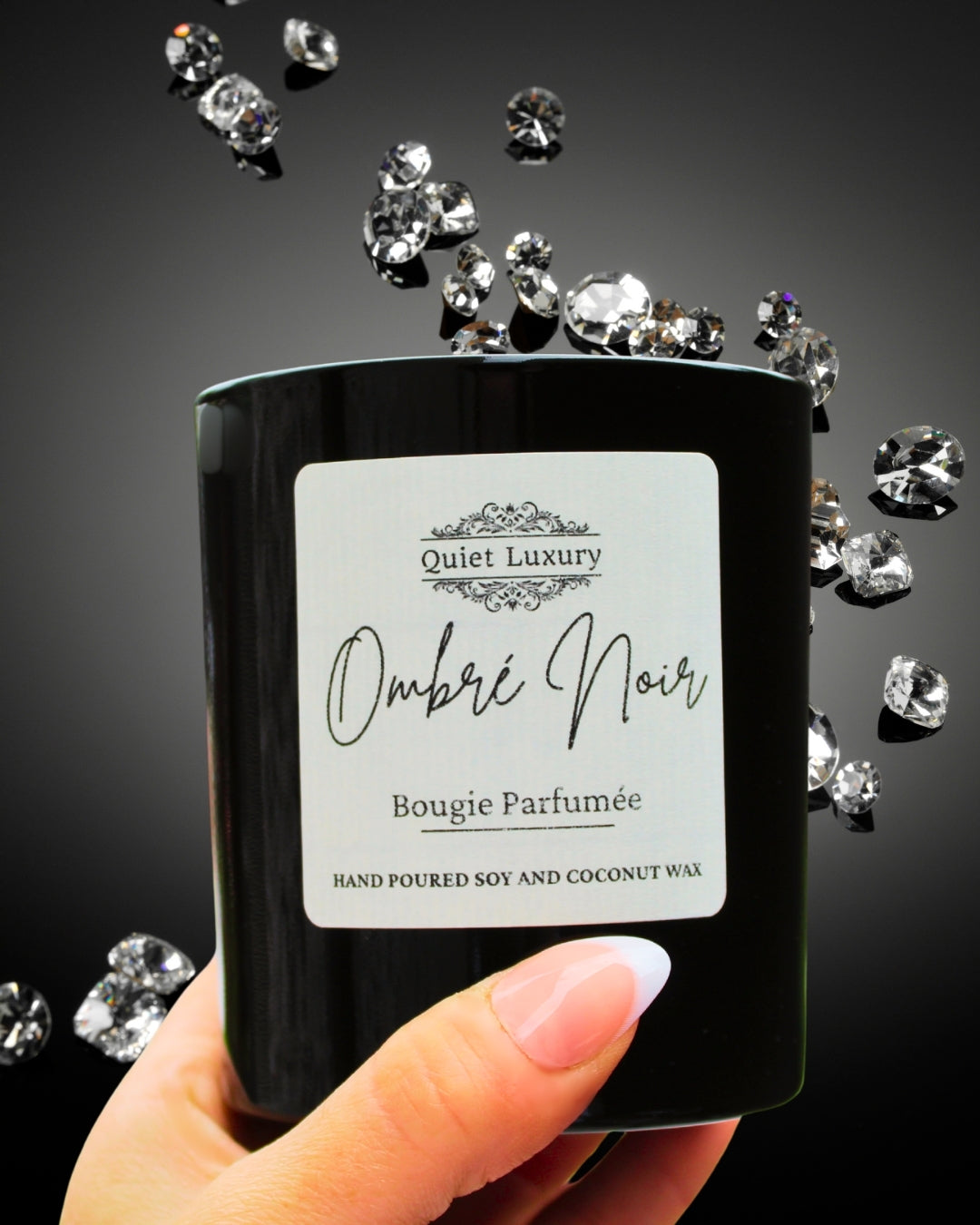 Black candle labeled 'Ombre Noir' from 'Quiet Luxury' held by a hand with diamonds falling around it.