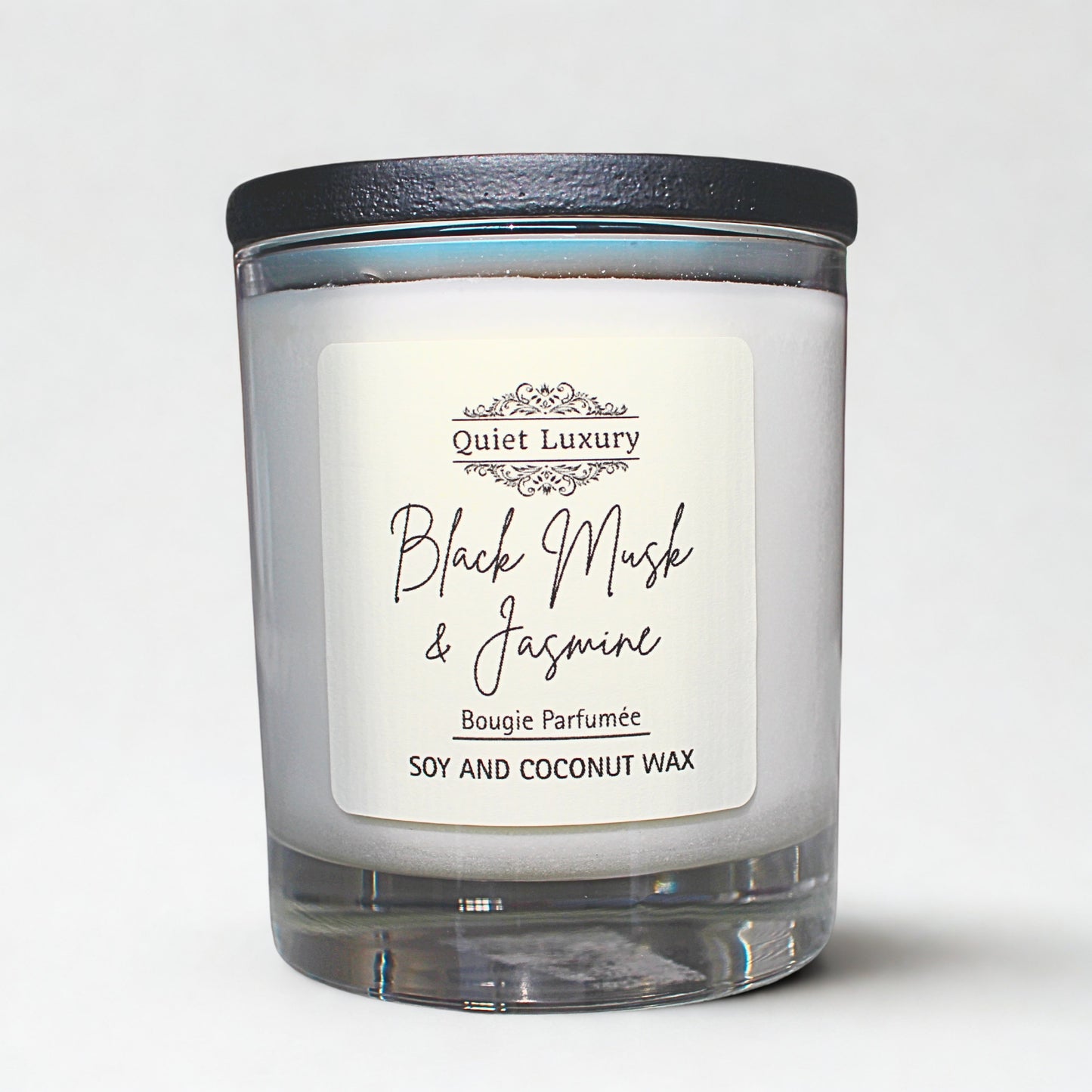 Candle with a label reading 'Quiet Luxury Black Musk & Jasmine' on a white background