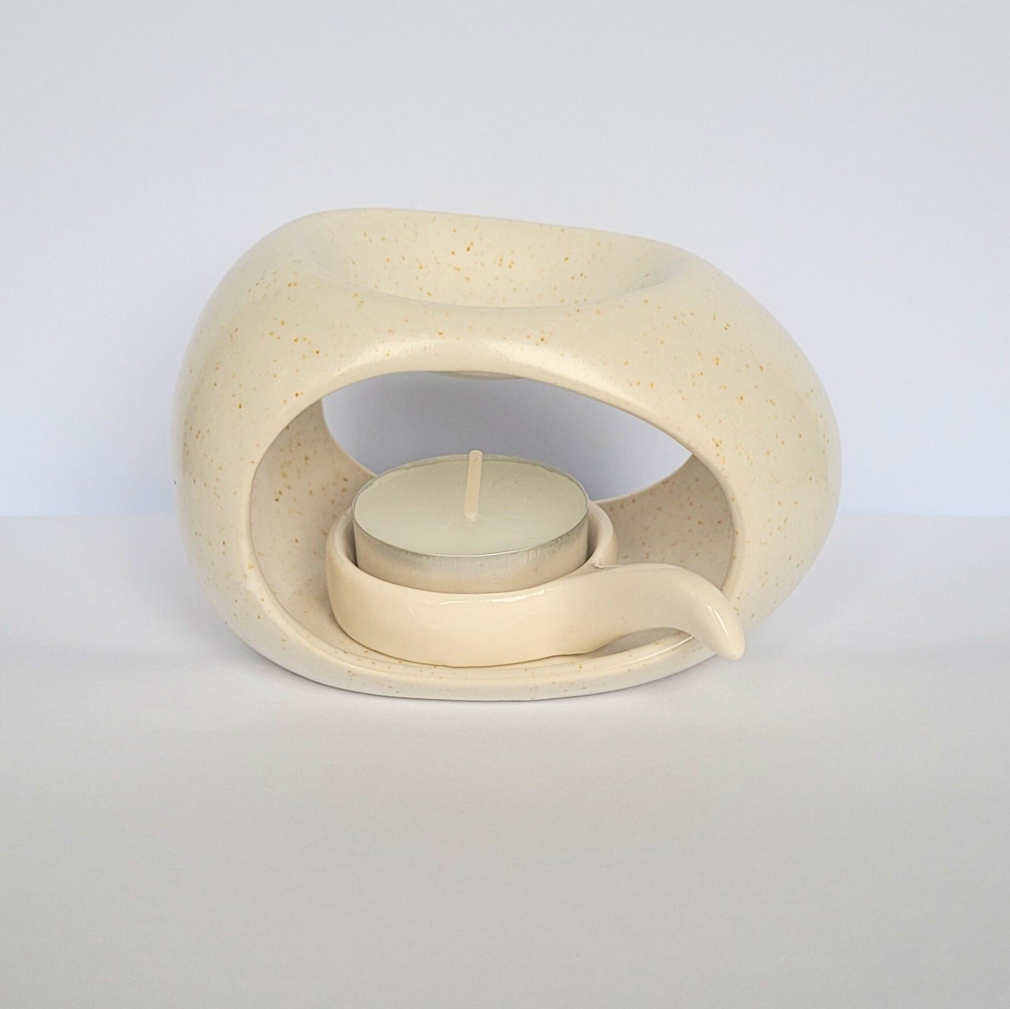 Beige ceramic wax warmer with a small candle inside on a light gray background