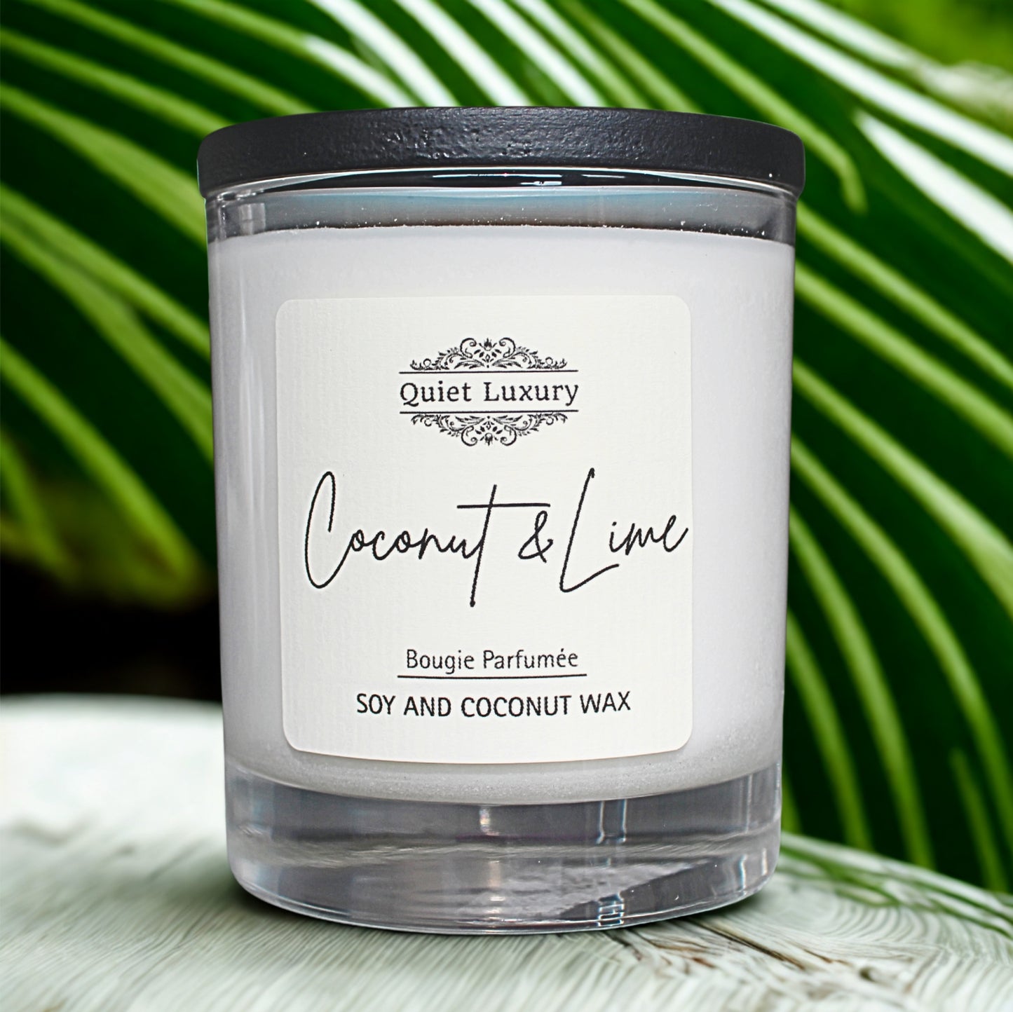 Candle with a label reading 'Quiet Luxury Coconut & Lime' on a green leafy background