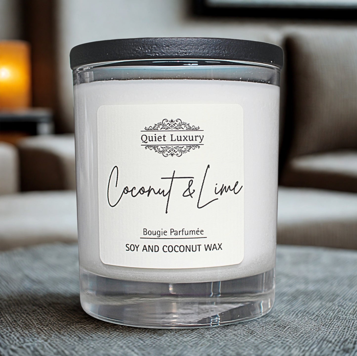 Candle labeled 'Quiet Luxury Coconut & Lime' on a textured surface with a blurred background