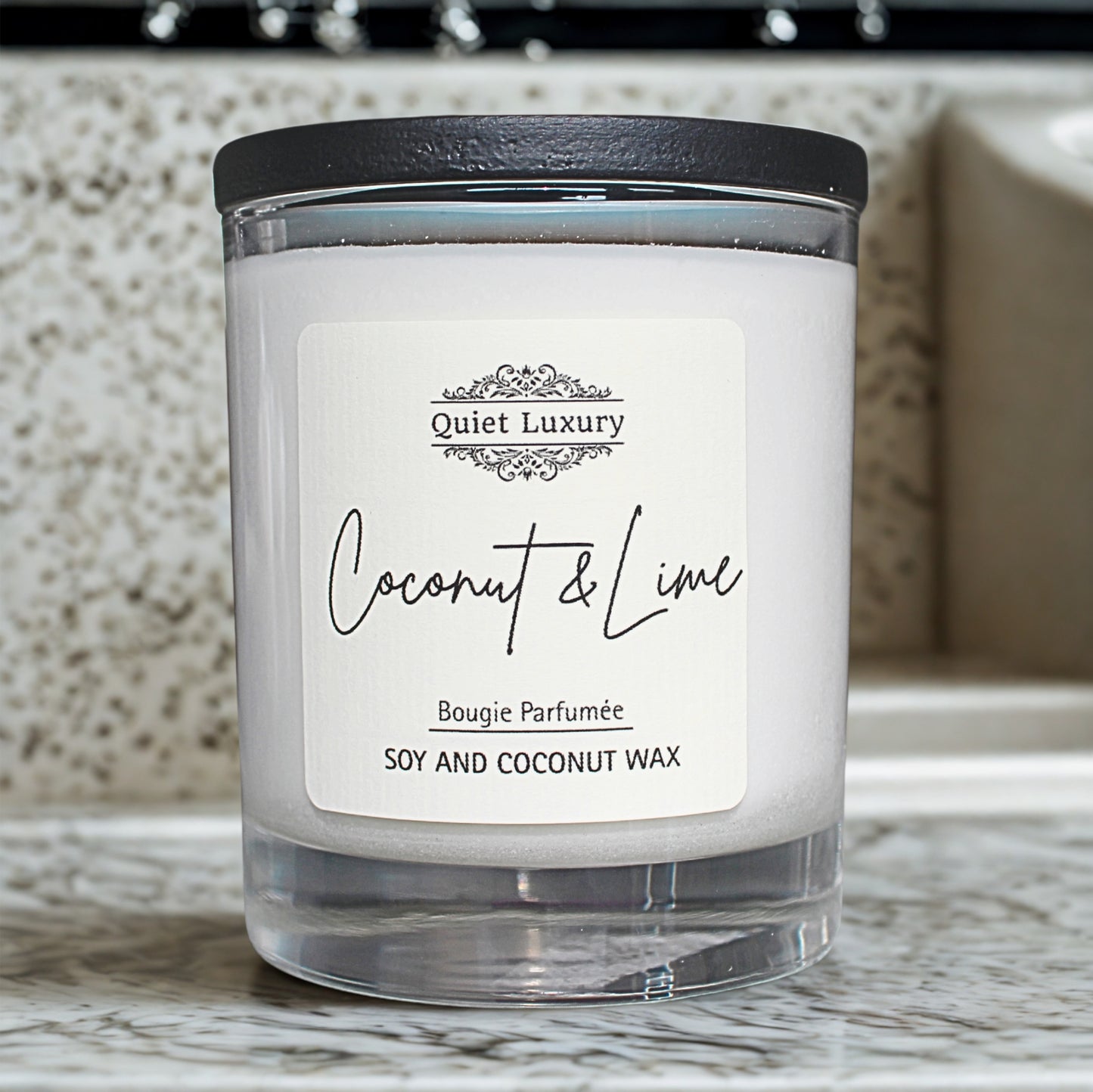 Candle with a label reading 'Quiet Luxury Coconut & Lime' on a marble surface.