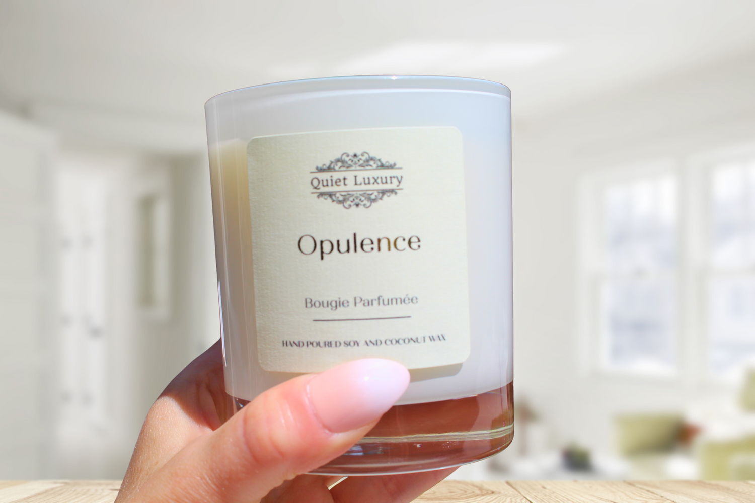 Hand holding Opulence scented soy and coconut wax candle in a glass jar indoors