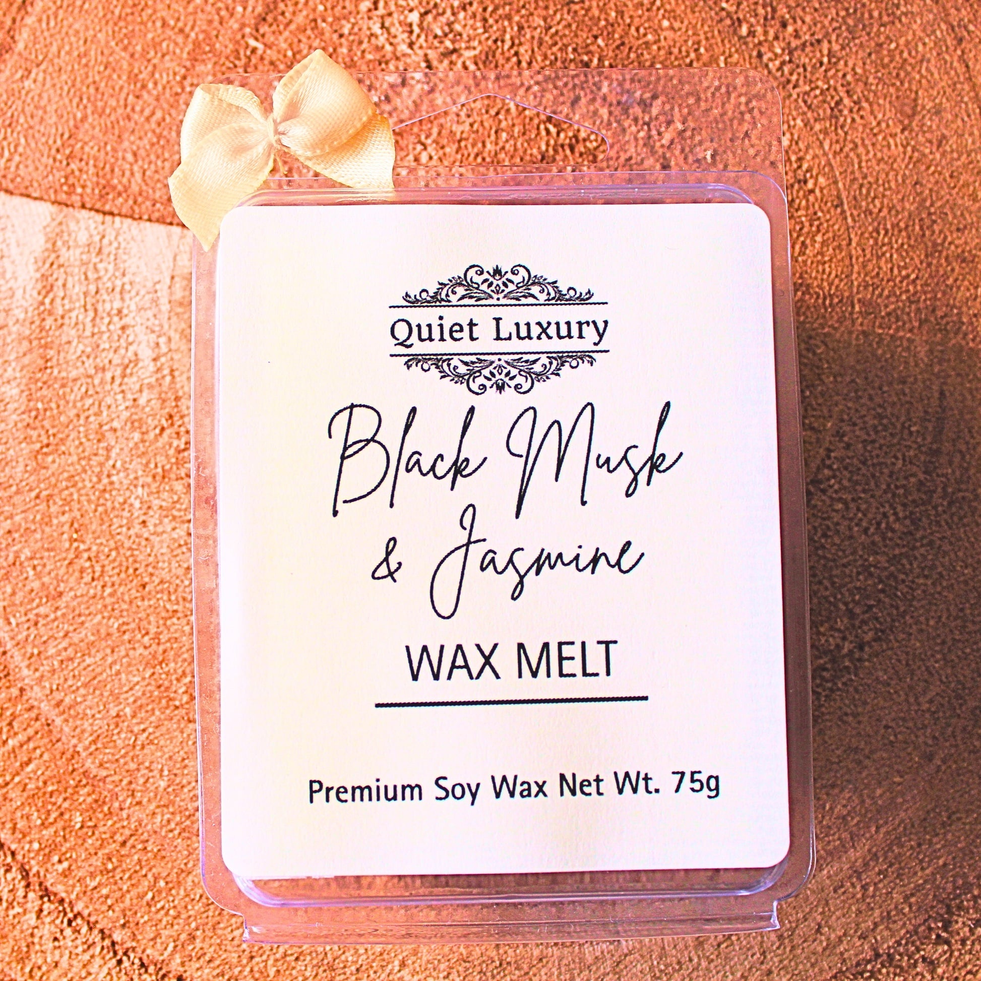 black musk and jasmine soy luxury wax melt packaging with 'Quiet Luxury' branding on a textured orange surface