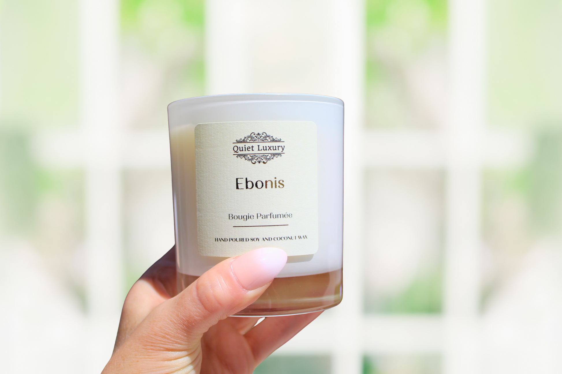 Candle labeled 'Ebonis' held by a hand with a blurred natural background