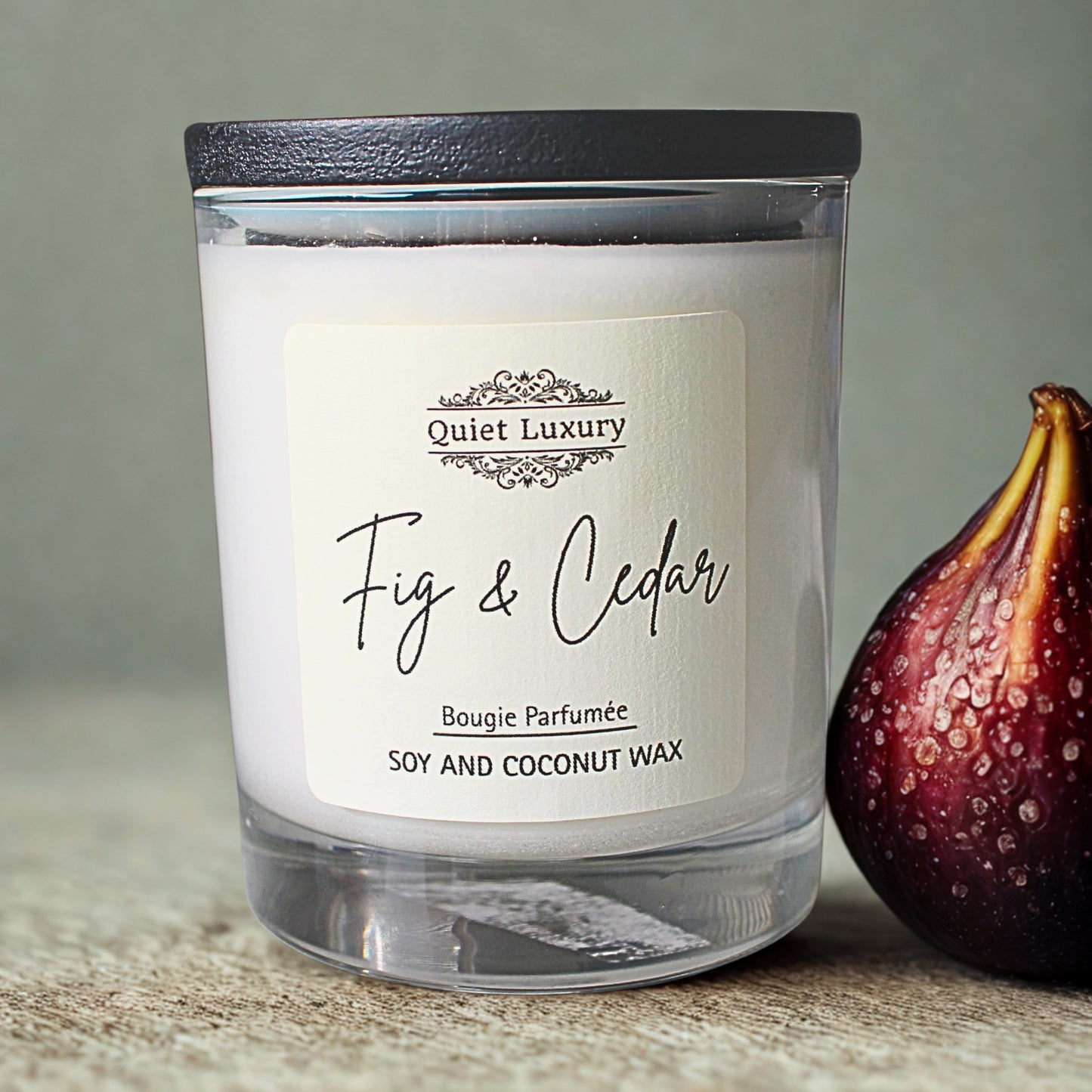 Candle labeled 'Fig & Cedar' by Quiet Luxury with a fig next to it on a neutral background
