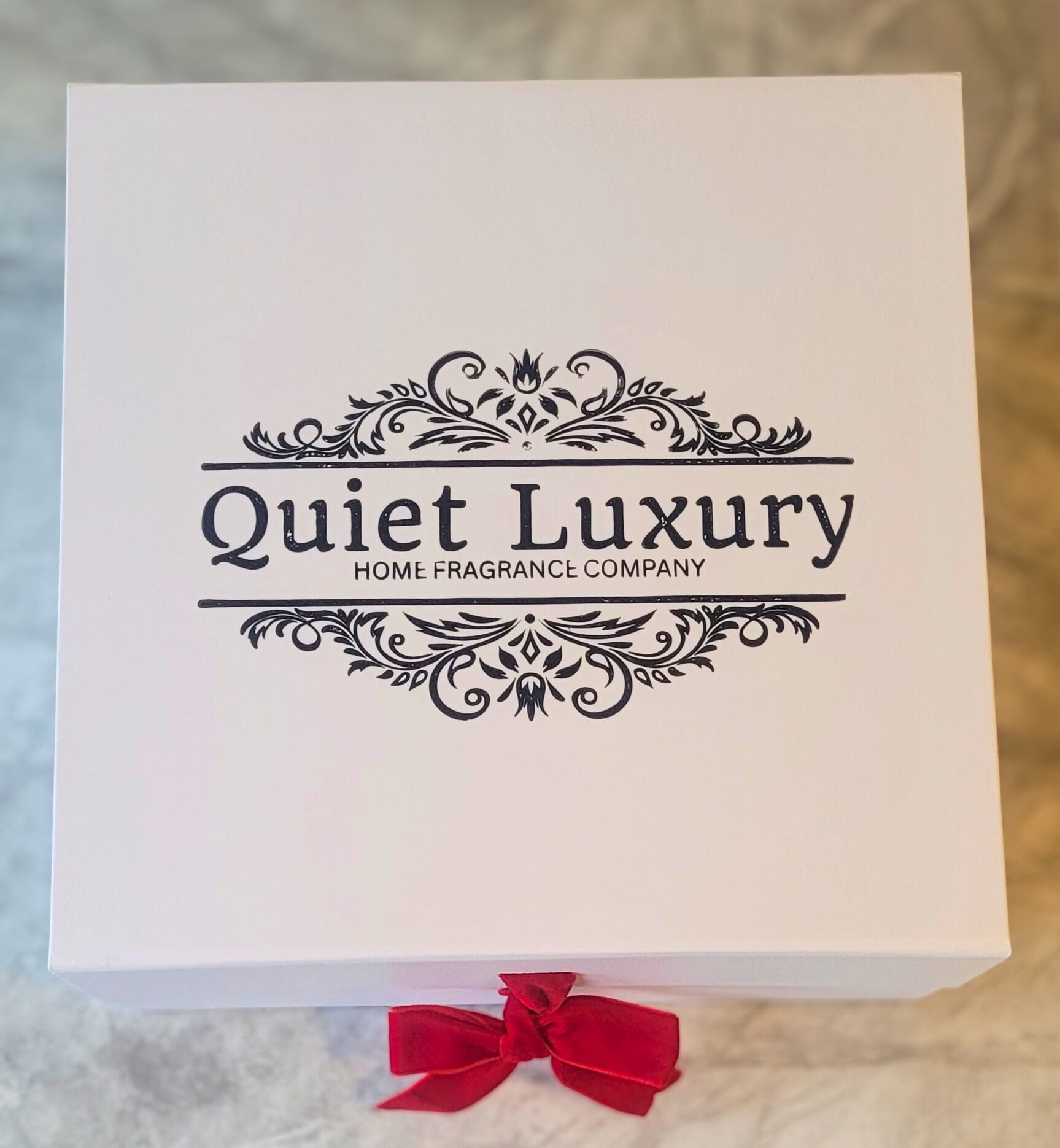 White box with 'Quiet Luxury' branding and a red bow on a textured surface