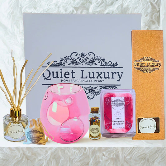 Pink wax melt diffuser and wax melts in front of a gift box with 'Quiet Luxury' branding on a textured white background