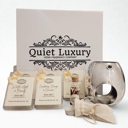 Quiet Luxury home fragrance products including wax melts and a candle holder on a white table with a branded white gift box in the background