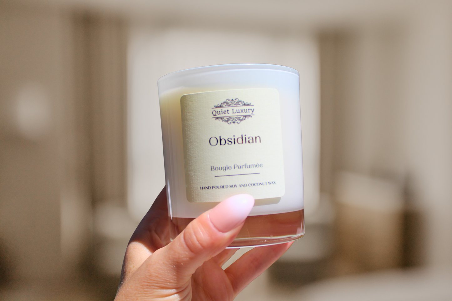 Hand holding a candle labeled 'Obsidian' with a blurred background