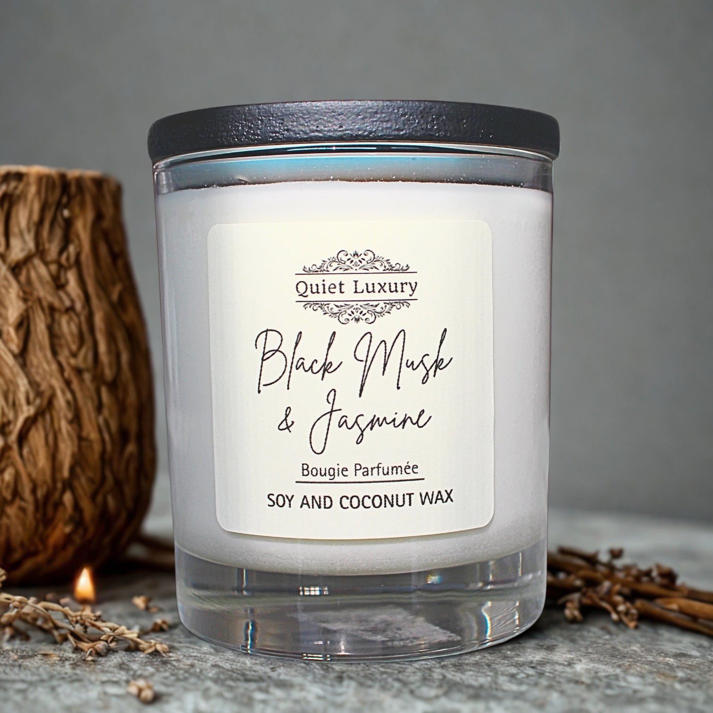 Candle with a label reading 'Quiet Luxury Black Musk & Jasmine' on a gray background.