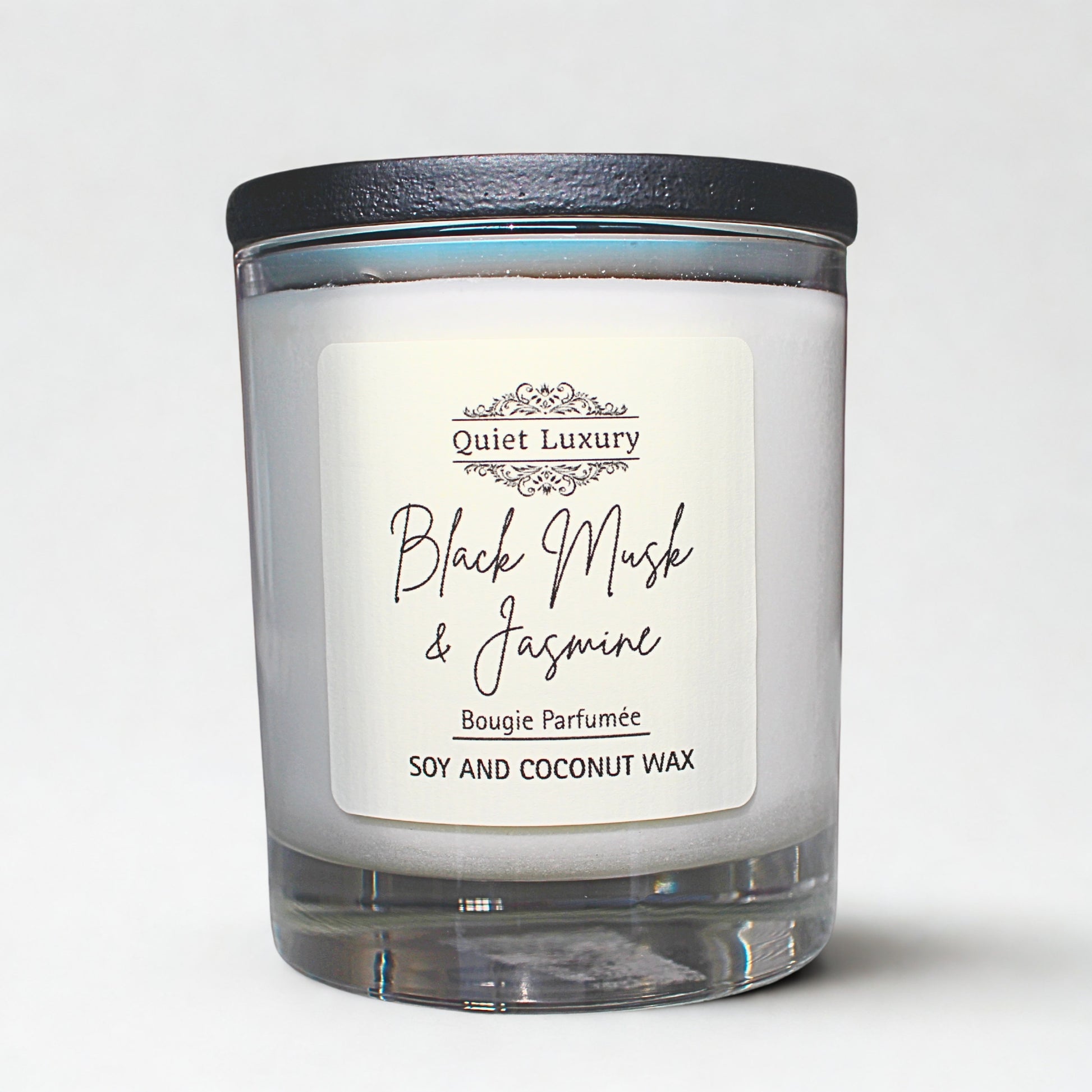 Candle with a label reading 'Quiet Luxury Black Musk & Jasmine' on a white background