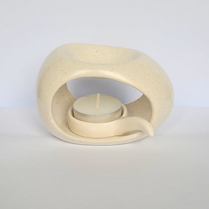 Beige ceramic wax warmer with a small candle inside on a light gray background
