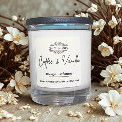 Coffee and vanilla luxury candle in glass jar with creamy white wax, surrounded by soft white flowers.