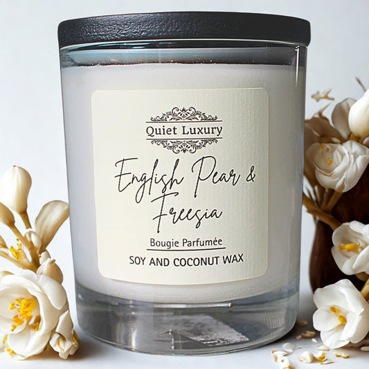 Candle labeled 'Quiet Luxury English Pear & Freesia' with floral decorations on a light background