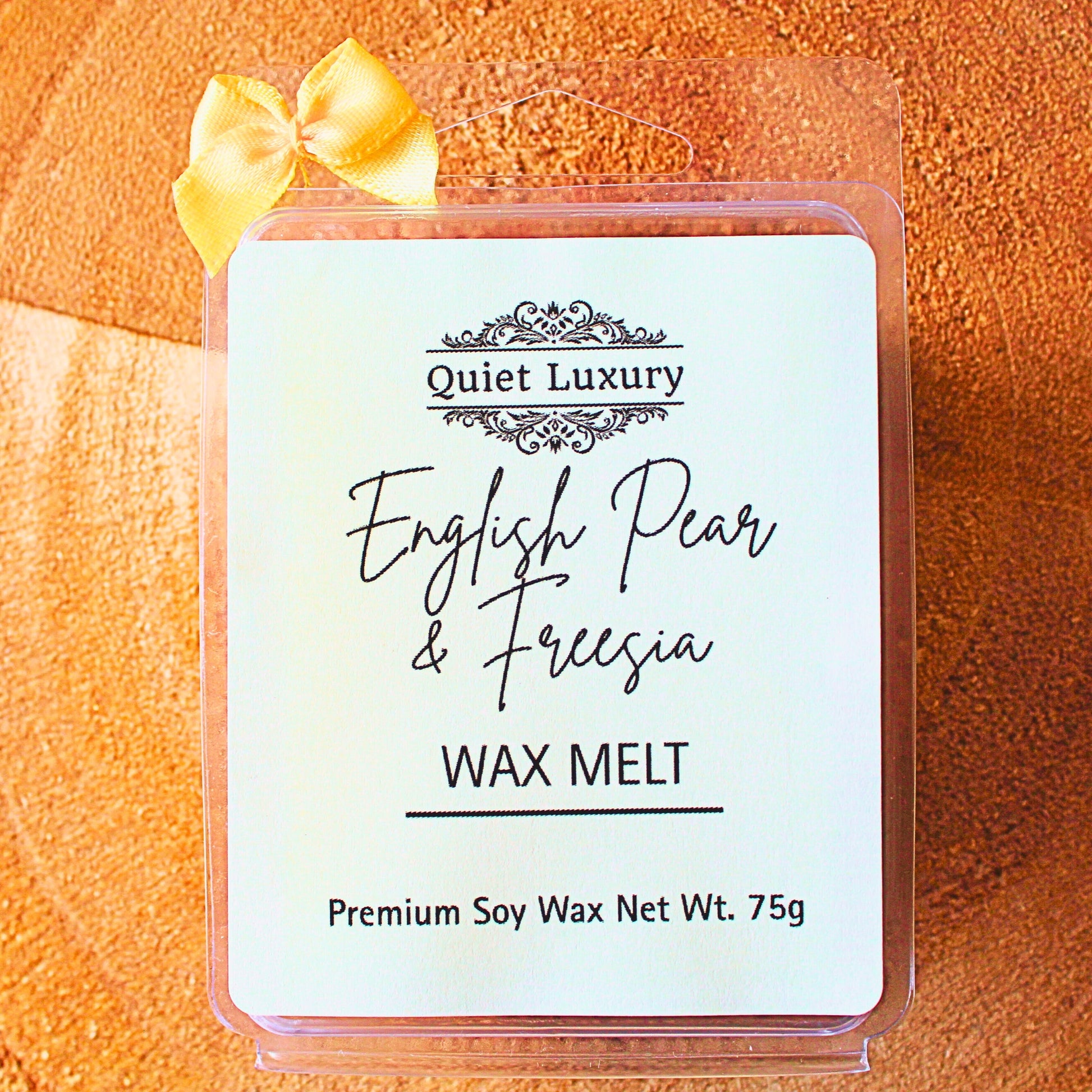 soy wax melt english pear and freesia melt with 'Quiet Luxury' branding on a textured orange background