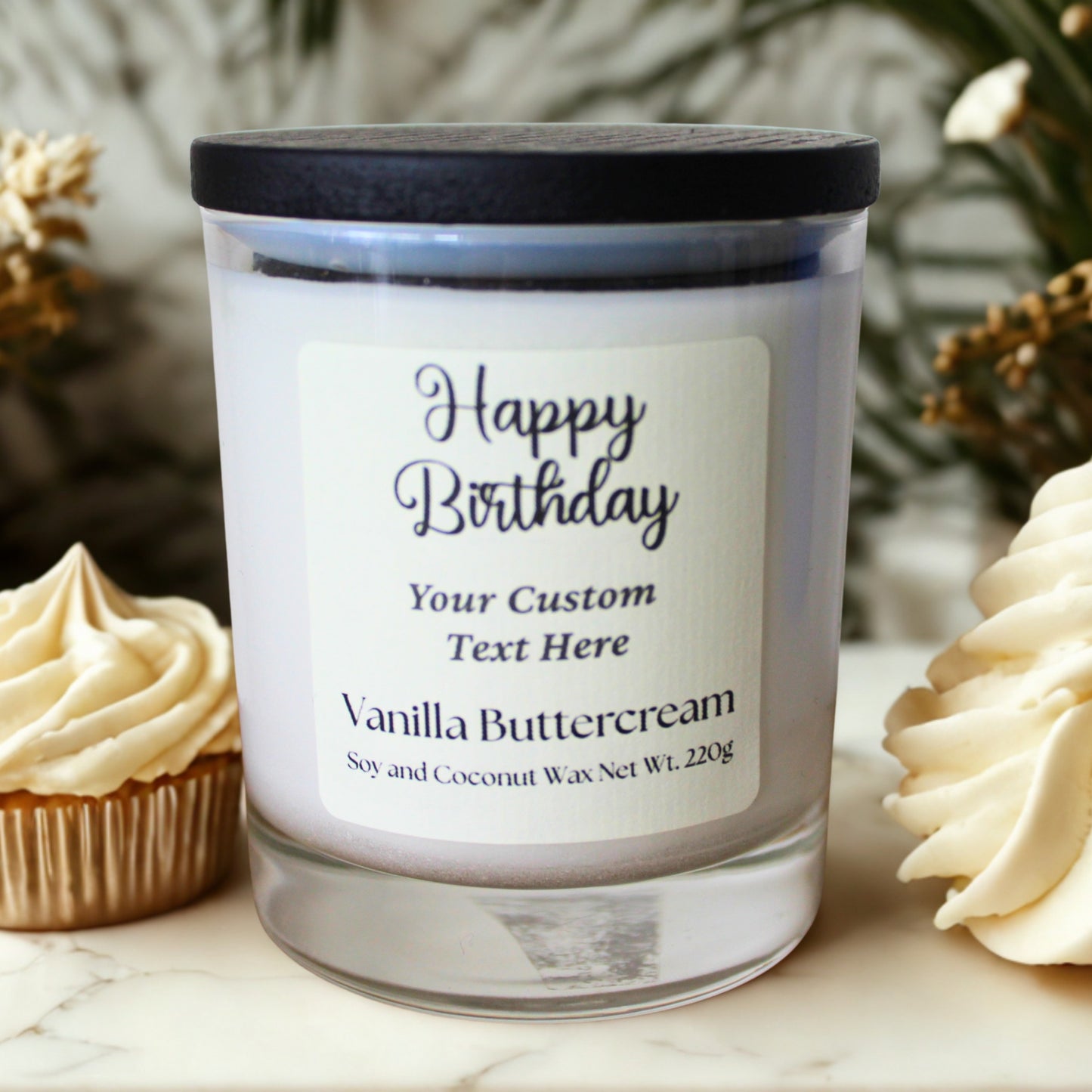 Personalized birthday candle with vanilla buttercream flavor next to cupcakes on a marble surface.