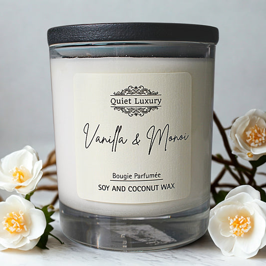 Candle labeled 'Quiet Luxury Vanilla & Monoi' with white flowers in the background
