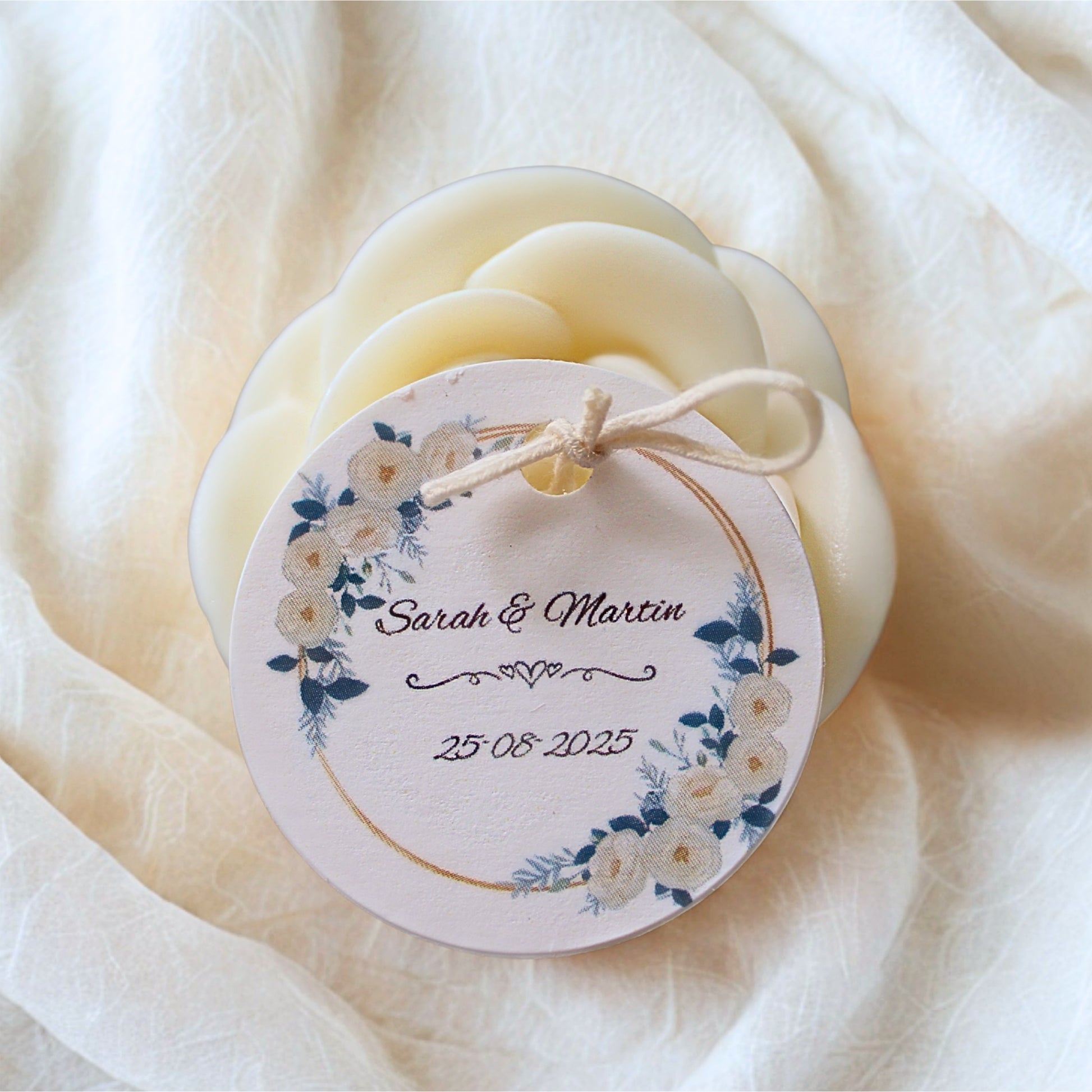 candle wedding favour with a decorative tag featurin personalised tag, on a soft white fabric background.
