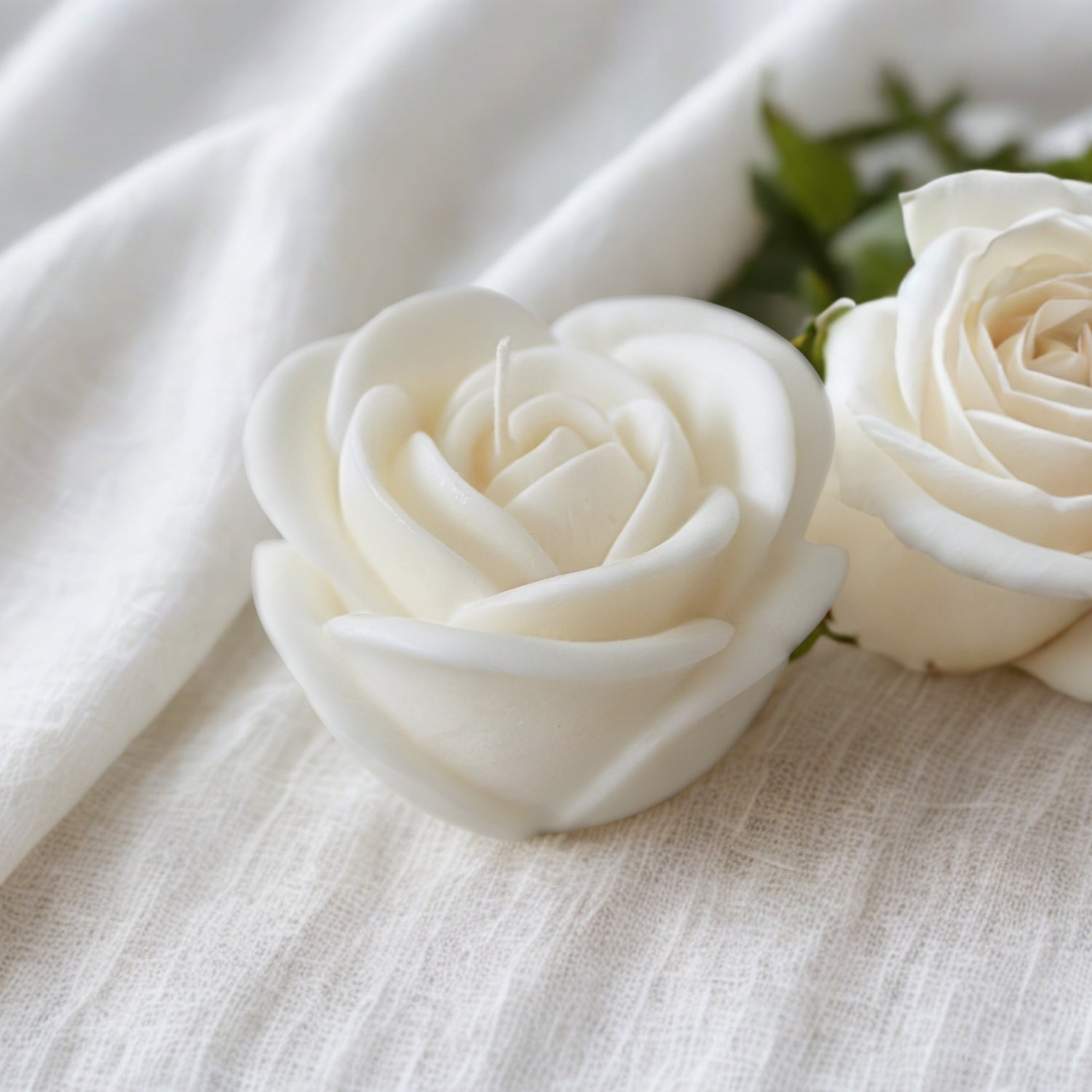Two white rose wedding favours on a textured white fabric background